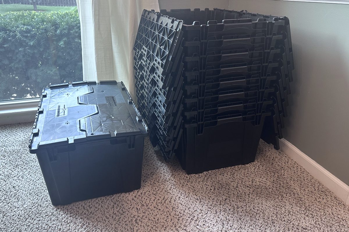 One assembled JoCo Bin Co moving bin beside a nested stack of collapsed bins in a room corner